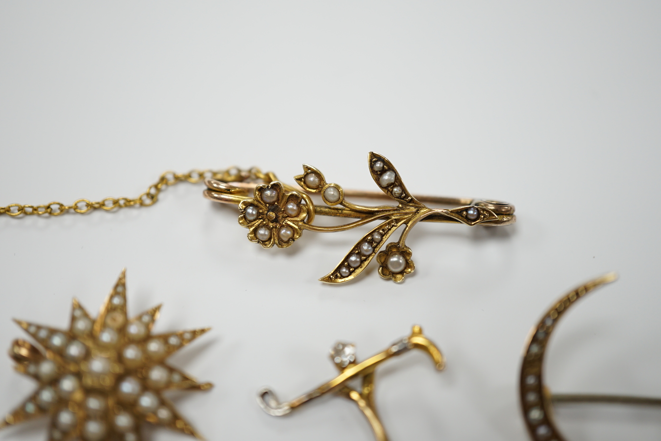 Three early to mid 20th century yellow metal and seed pearl set brooches, largest 34mm, two similar stick pins and a diamond set riding crop stick pin.